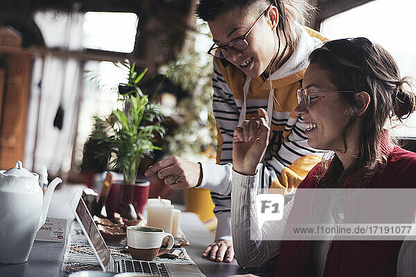 zwei queere Geschäftsfrauen lachen und arbeiten gemeinsam am Laptop zu Hause