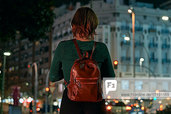 Rückenansicht einer jungen Frau mit Rucksack in einer nächtlichen Stadt
