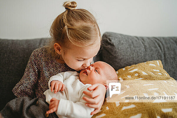 Schönes weißes Mädchen küsst neugeborenes Baby Bruder auf der Couch zu Hause