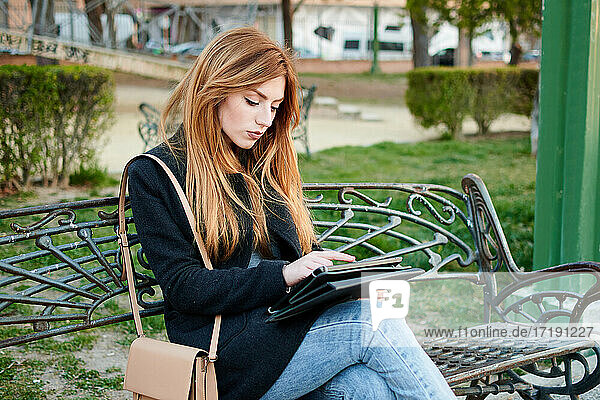 An attractive young woman is looking at her tablet in a park