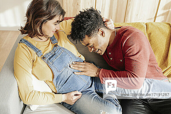 Schwarzer Mann berührt den Bauch einer schwangeren Frau zu Hause.