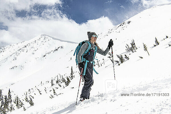 Lächelnde junge Frau mit Rucksack beim Skifahren auf einem schneebedeckten Berg im Urlaub