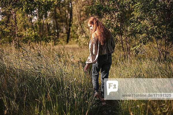 Rückenansicht von Teenager-Mädchen berühren Gras zu Fuß auf dem Weg im Sommer