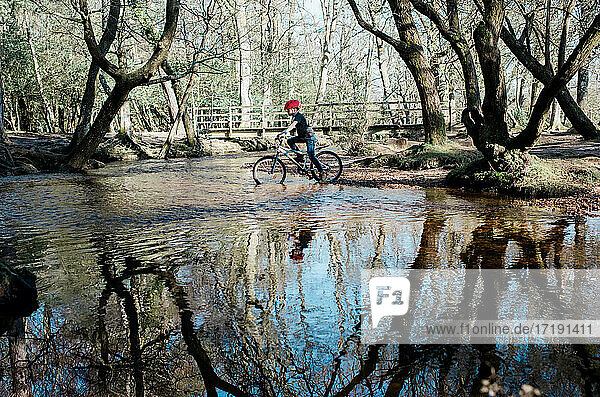 young boy cycling through a river to cross whilst mountain biking