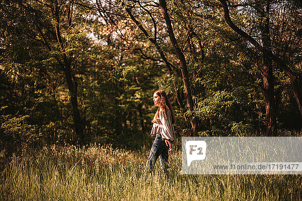 Teenager-Mädchen geht durch grünes Gras im Wald im Sommer