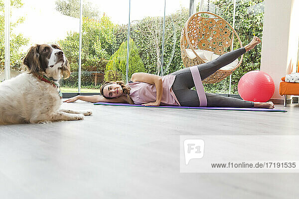 Frau mit ihrem Hund macht Beine Übung mit Laufband  Fitness zu Hause