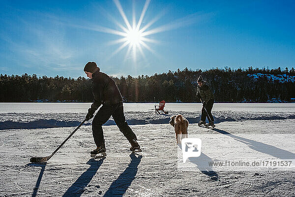 Father and son playing hockey on outdoor rink on frozen Canadian lake.