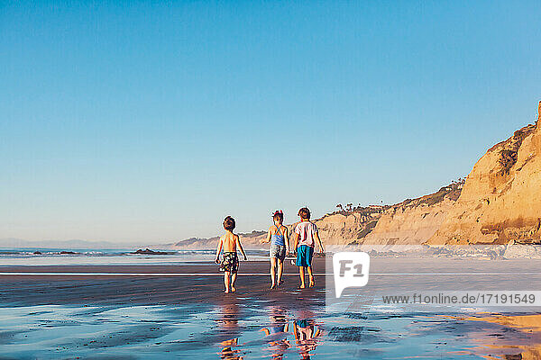 Drei kleine Kinder  die bei Ebbe und Sonnenuntergang am Strand spazieren gehen.