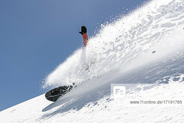 Mann Snowboarding auf schneebedeckten Berg gegen klaren Himmel