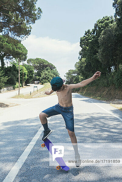 Portrait of cheerful shirtless teen skateboarding on mountain road
