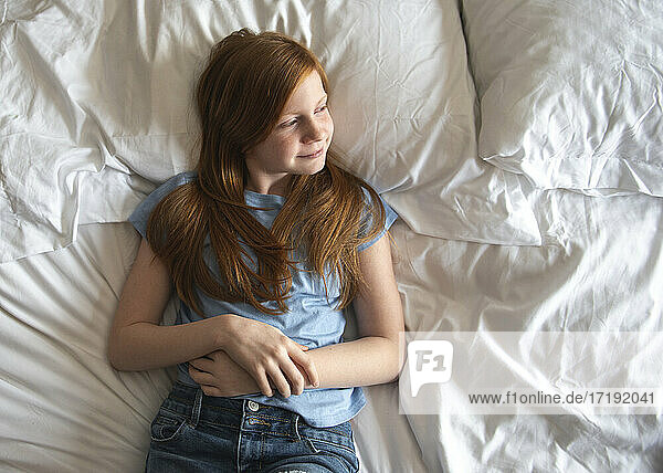 Young happy red haired blue eyed girl laying on white bed.