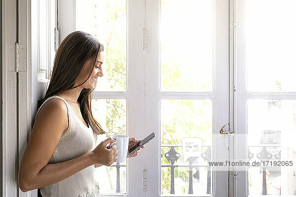 Lächelndes Mädchen trinkt Kaffee und liest oder schreibt auf ihrem Handy