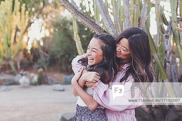 Asiatische Mutter umarmt ihre Tochter im Vorschulalter und bringt sie zum Lachen.