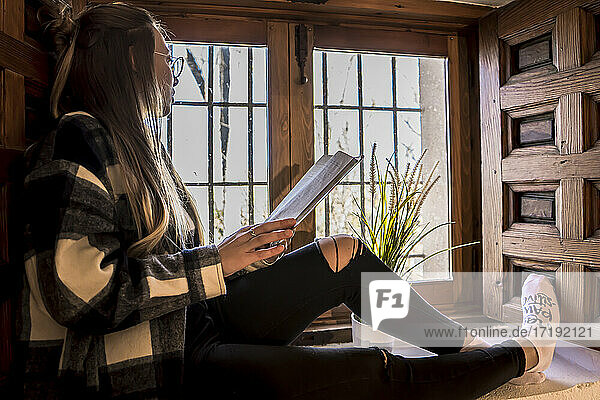 Frau liest ein Buch bei einer Tasse Tee am Fenster