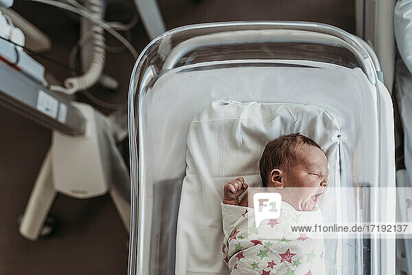Newborn baby boy in bassinet wrapped in hospital blanket yawning