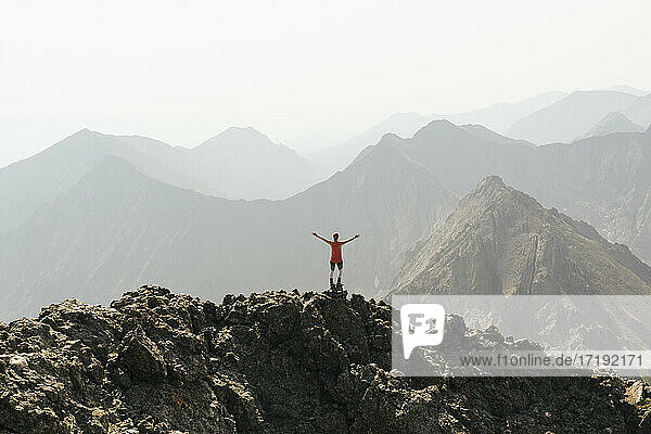 Frau steht mit ausgestreckten Armen auf dem Gipfel eines Berges gegen den klaren Himmel