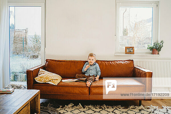 Adorable weißen blonden Jungen sitzen auf der Couch mit Bleistift in seiner Nase