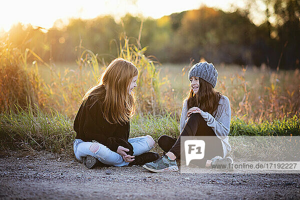 Zwei hübsche junge Mädchen in Pullovern sitzen im Herbst draußen.