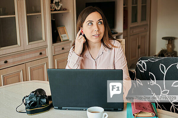 Junge Frau arbeitet von zu Hause aus an ihrem Laptop. Sie benutzt einen Kopfhörer