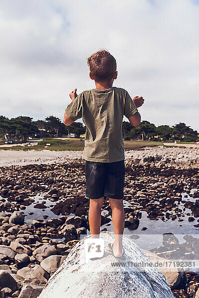 Junge auf dem Gipfel eines Felsens am Meer - mit dem Rücken zur Kamera.
