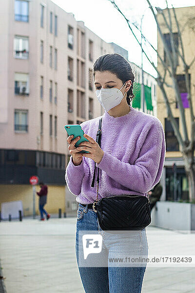 young woman with KN95 protective mask on the street watching mobile