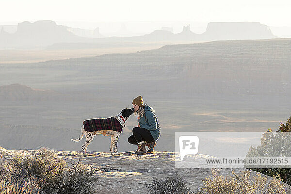Junge Frau küsst Hund auf Berggipfel in der Wüste im Urlaub