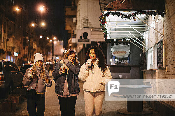 Junge Frauen mit Einwegbechern auf der Straße in der Stadt bei Nacht