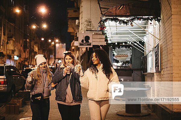 Freundinnen mit heißen Getränken auf der Straße in der Stadt bei Nacht