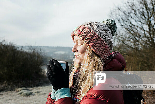 Frau lächelt mit einem heißen Getränk in der Hand  während sie die kalte Luft im Vereinigten Königreich genießt