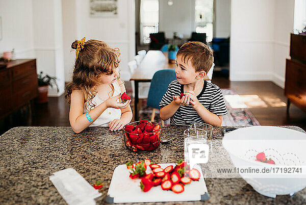 Bruder und Schwester teilen sich frisch geschnittene Erdbeeren an der Kücheninsel