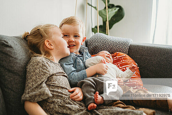 Adorable brother and sister holding baby on couch at home during covid