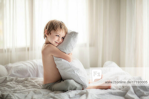 Kleiner Junge auf einem Bett mit einem Kissen