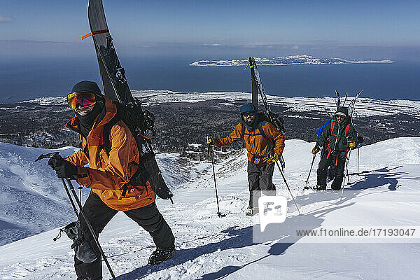 Männer mit Skistöcken beim Klettern auf einen schneebedeckten Berg im Urlaub