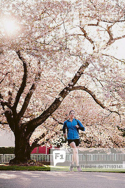 Sportliche Frau läuft im Stadtpark vor einer großen Kirschblüte