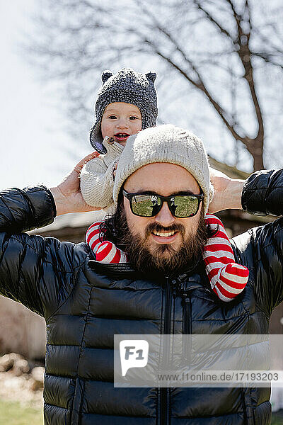 Happy baby on dad's shoulders in backyard on chilly afternoon