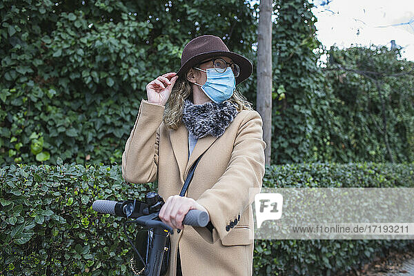 Blond woman with hat and mask  consults her phone and uses her electri