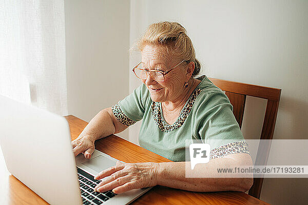 Ältere Frau lächelt  während sie zu Hause an ihrem Computer arbeitet