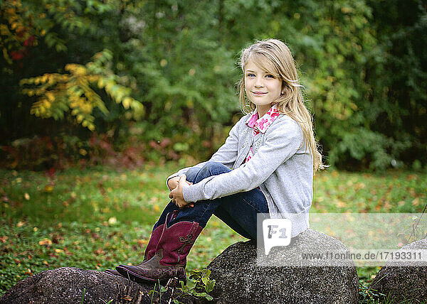 Junges blondes Mädchen in roten Cowboystiefeln  das draußen auf einem Felsen sitzt