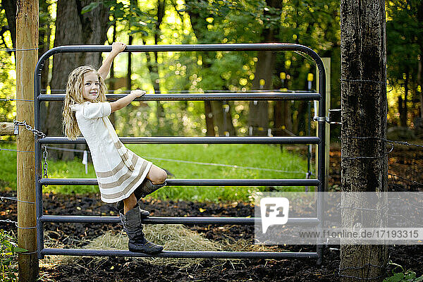 Kleines blondes Mädchen klettert auf dem Bauernhof über ein Tor.