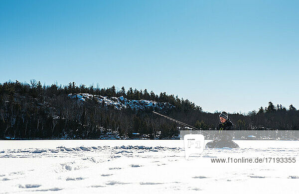 Jugendlicher Junge beim Eisfischen auf einem zugefrorenen See in Kanada an einem Wintertag.