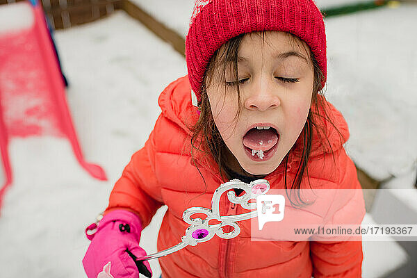 Junges Mädchen probiert Schnee und hält Spielzeugstab an einem Wintertag
