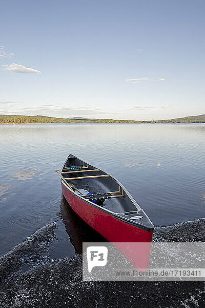 Rotes Kanu am felsigen Ufer eines unberührten  ruhigen Sees in Maine