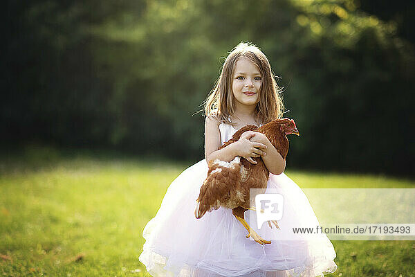 Niedliches kleines Mädchen hält ein Huhn im Freien im Gegenlicht.