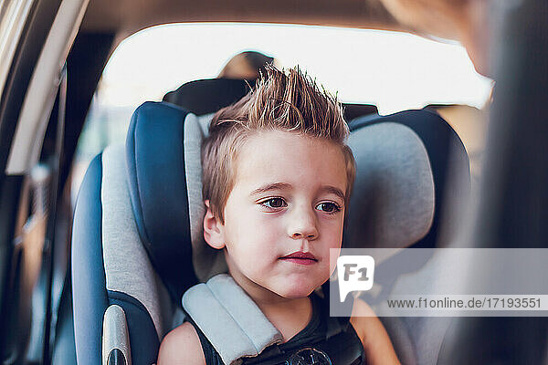 Preschool age boy sitting in car seat inside a car.