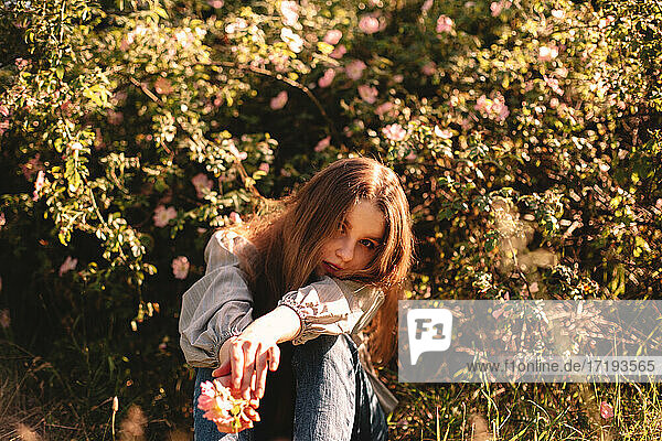 Teenager-Mädchen sitzt im Sommer inmitten von Blumen im Park