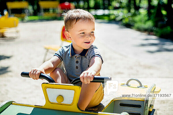 Adorable 2 Jahre alt Kind Reiten hölzernen Auto im Sommer Park Spielplatz