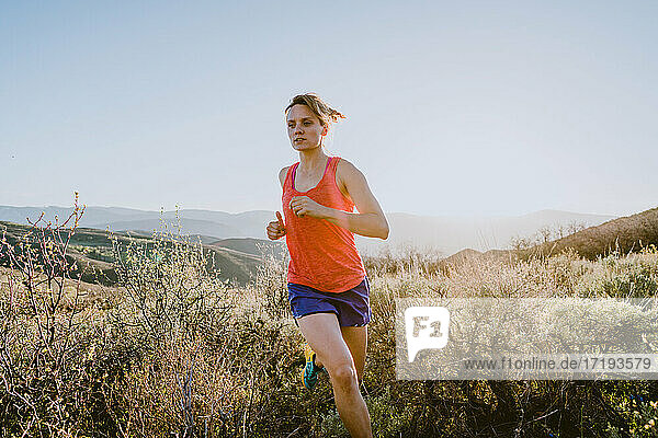 Athletic blonde woman trail runs in the mountains at golden hour