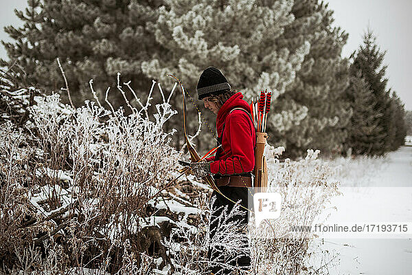 Teen boy looking at animal trap in winter Wisconsin with bow and arrow