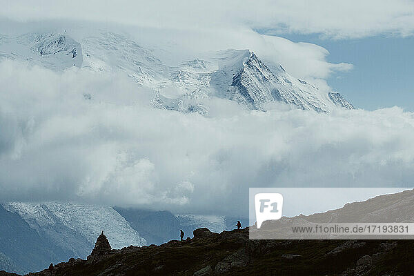 Zwei Wanderer wandern in der Ferne zwischen Wolken und verschneiten Gipfeln