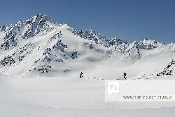 Side view of men with splitboards walking on snow covered mountain against clear sky